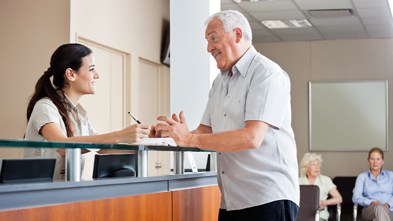 Older white haired man talking to receptionist