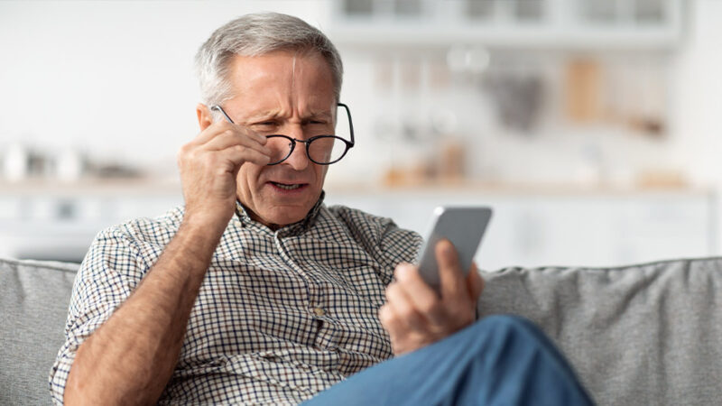 Older man struggling to see through reading glasses, looking at his phone