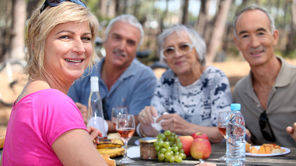 A group of middle-aged friends hanging out in a park with food on the table.