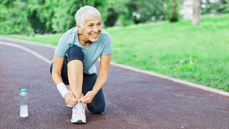 "Tanned older woman tying shoe laces after running, on a running track"