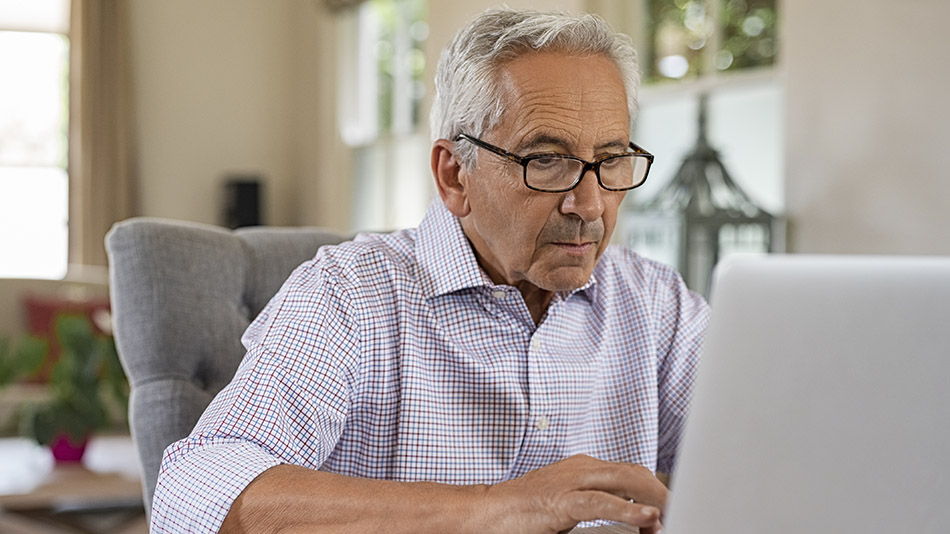 Senior man with white hair and glasses using his laptop